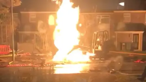 A digger is on fire with a bright orange flame on residential street