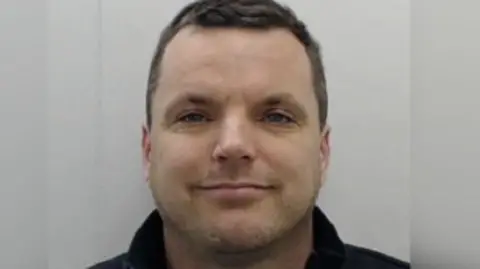 Man smiles at camera in mugshot.