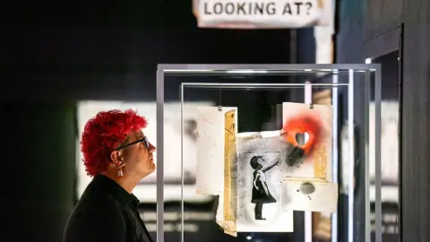 A gallery steward examines the girl with a heart balloon artwork at the Banksy Cut & Run exhibition in Glasgow