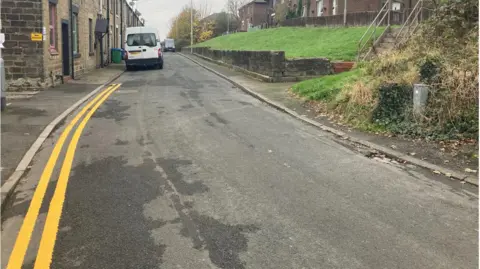 LDRS Double yellow lines running along Major Street in Milnrow. Homes line both sides of the street and several cars are parked up.