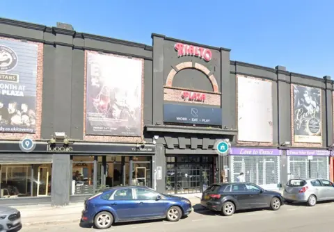 The Rialto Plaza sign on the outside of the Moseley Avenue building is red and features a semi circle brick work design. It appears to be quite a big venue above several shops including a dance studio. There are posters of Elvis Presley and George Michael tribute nights.