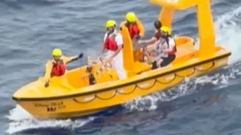 A small yellow rescue boat in the sea with people on it.