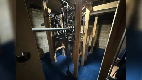 Church clock mechanism. Cogs supported by a metal frame and a wooden support which raises it from the floor.