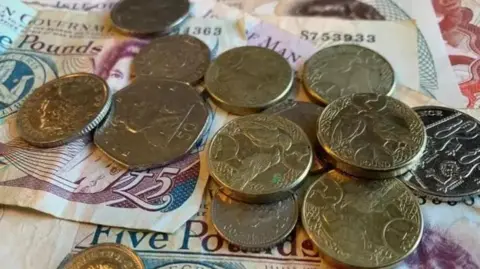 Silver and gold coloured coins placed on top of some Manx £5 notes.