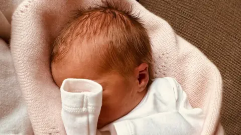 PA Media Baby girl Athena is pictured in a close-up photograph showing most of her head, with her hand covering much of her face. 