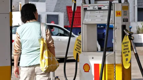 A woman looks at signs displayed on empty fuel dispensers at a Shell petrol station that ran out of fuel, in Sydney, Australia, March 30, 2026.