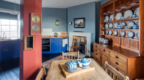 The Landmark Trust The image shows the inside of a house, with cutlery on the table and a sink and cupboard in the background. A fireplace can also be seen.