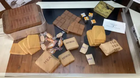 BBC Supplies including meat and oat in brown paper packages, biscuits and toilet roll with mess tins