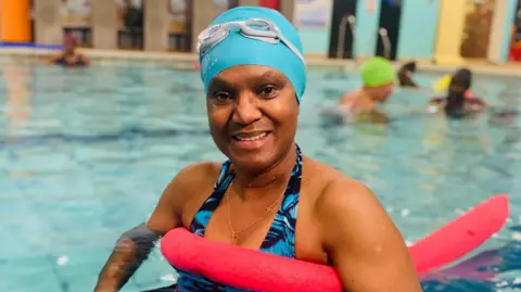 Fola Oluwaremi in the pool wearing a light blue swim cap and holding a red float under her arms 