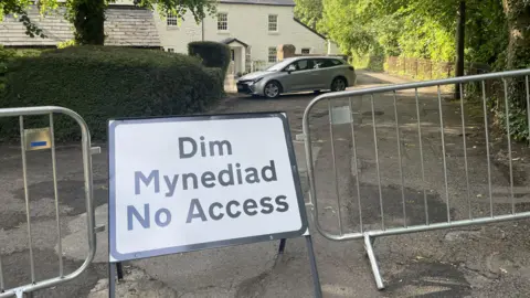 A no access sign linking barriers in front of a house with a silver car parked outside.