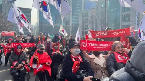 Yoon supporters gathered outside the courthouse, many waving South Korea flags and holding red banners that read: "Yoon, again! Make Korea great again." Some wore red scarves and shawls.