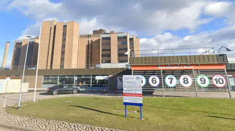 The front entrance to Raigmore Hospital with signs showing numbers and colours of different zones inside the large building.