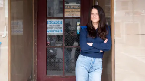 Andrew Porter Kate Bolger stands with her arms crossed in front of a door