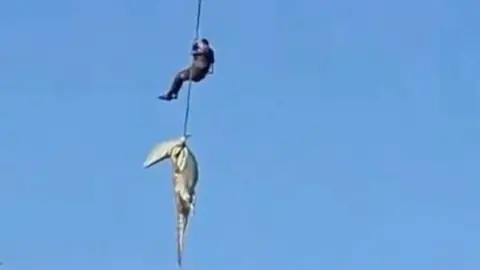 South Africa Police Service A grainy screen grab showing a rope with a crocodile on the end with a man holding on higher up