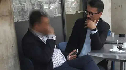 Police handout Mark Acklom at a cafe in Geneva sitting with another man. They are both wearing suits
