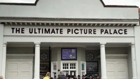 People gathering in front of the Ultimate Picture Palace on an overcast day.