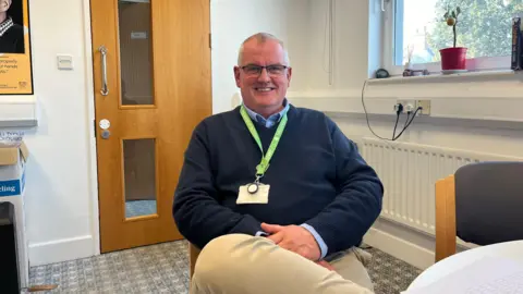 Chris Torode sitting in an office, wearing a navy jumper and a TGI lanyard.