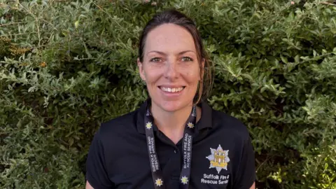 Alison Borrman is wearing a shirt with the Suffolk Fire and Rescue Service badge and logo. She smiles at the camera.