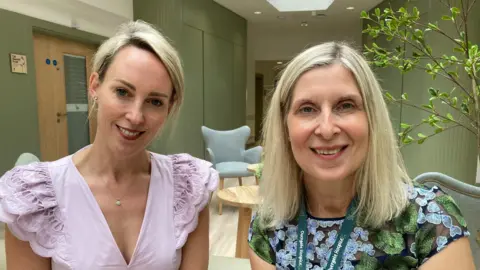 BBC/Cara Thorpe Jessica Roche and Tracey Wilcocks are pictured. Jessica is on the left, wearing her blonde hair up and wearing a light pink top. Tracey is on the right. She has blonde hair down to her shoulders and is wearing a flowery top and a dark green lanyard. Both are smiling