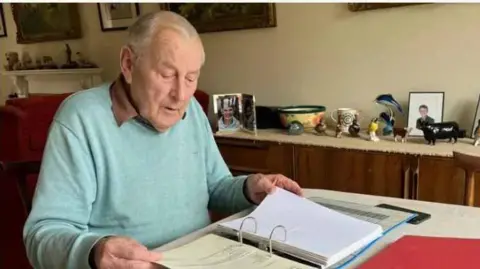 Peter Walker sits at home, working at his dining room table surrounded by files from his campaign.