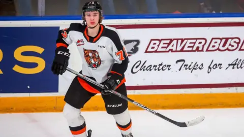 Gavin McKenna pictured playing hockey. He wears a helmet and a black, white and orange uniform with a tiger on it