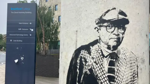 BBC/Grace Wood A graffiti image of David Hockney on a pillar. Behind in a sign showing directions around Bradford College