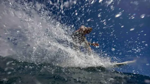 A surfer performs a cutback on a critical section of a wave creating a spray of water as they head back to the pit with a look of satisfaction and joy on their face.