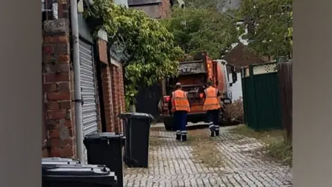 A Middlesbrough Council bin wagon after an alleyway collection on Barker Road and Cambridge Road. Bins line the side of a cobbled alleyway and two bin men can be seen walking behind the lorry.