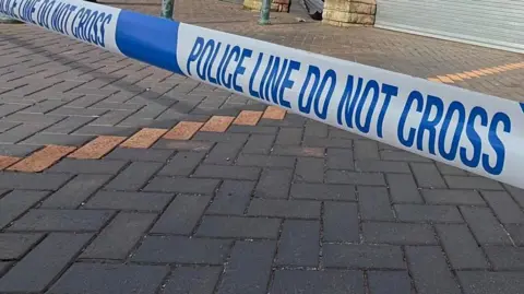 Police tape on pavement near shops