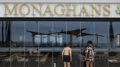 Two boys peering inside Monaghans bar in Costa del Sol. One of them is wearing black shorts and the other is wearing a long shirt covering his shorts.