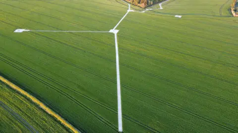 A very green and flat field which has silver coloured track laid across it in an inverted Y-shape. 