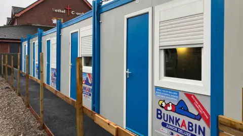 Five of the sleeper pods stretching into the distance. Each has a blue door and a window with white shutter.