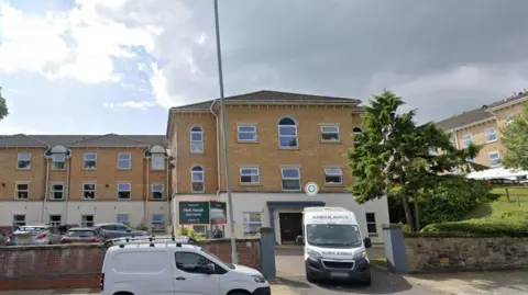 External view of Park House Care Home in Birkenhead showing an ambulance and driving out of the car park and a white transit van park in the street outside the entrance