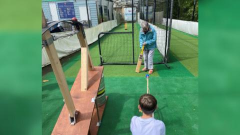 A youngster bowls towards an elderly person, who is holding a cricket bat
