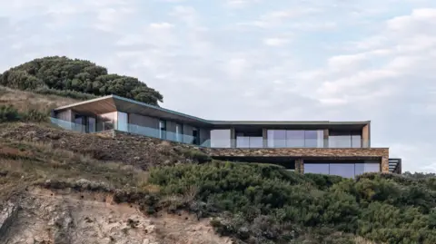 Rundell Associates A modern home built on to a cliff. It has large windows