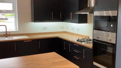 The new kitchen with black cupboards with long copper handles and wooden worktops.