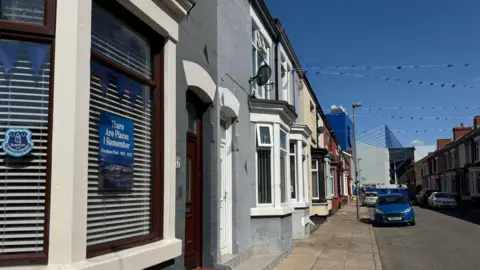 Jonny Humphries/BBC A sticker in the window of a terraced house which reads "There are places I remember" with a picture of Goodison Park, which is visible in the background.