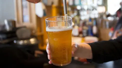 Getty Images A pint of beer being pulled in a bar with a blurry background. 

The hand is in vision with a black long sleeved arm.
