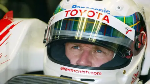 Getty Images Allan McNish in close up with a Toyota helmet on and tartan trim round it