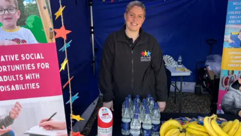 Megan wears a black fleece with a Special Stars logo on. She stands in front of bottles of water and bananas.