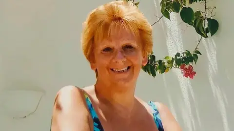 Woman smiling at the camera in a sunny scene with a white wall in the background