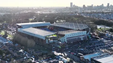 West Midlands Police An aerial view of Villa Park in Birmingham on a clear day, with the city's skyline visible in the background. Crowds of fans can be seen around the stadium and in nearby streets. The surrounding residential area and car parks are also visible.