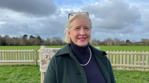 woman wearing blue rollneck and pearls standing in grass field 