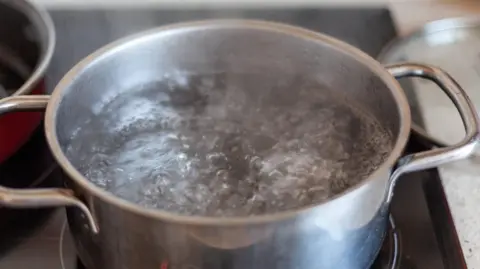 A metal pan of water boiling on a stove.