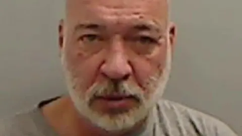 Mugshot of Hunt who is bald with a neat white beard and pitted complexion. The picture is blurry and very close up. 