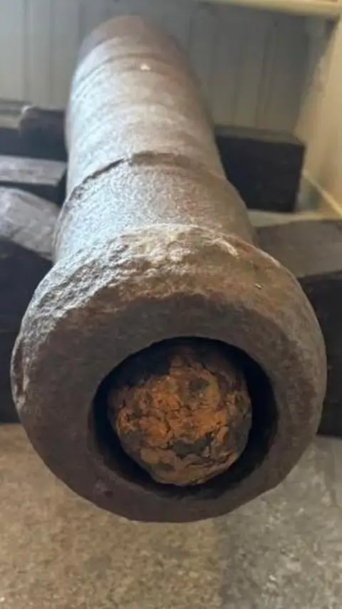 Historic Assynt A view down the length of one of the cannons. It is metallic brown in colour and has a cannonball placed at the end of it.