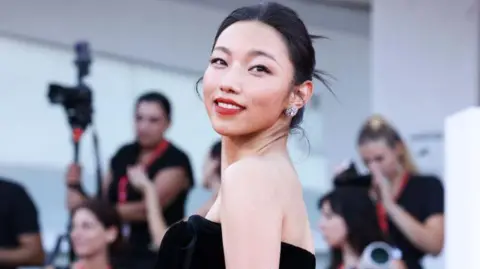 Nashi, turning her head, smiling, in a black dress