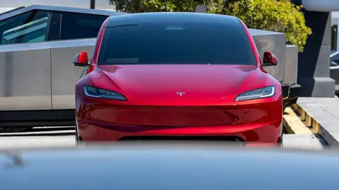 Getty Images Front-on view of a red Tesla sedan car in a car park.