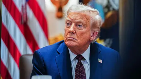 Getty Images Man sits in suit in front of American flag