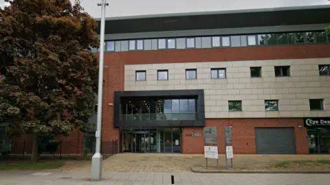Google The four-storey building has an exterior made of a mix of materials including grey metal, white stone and red brick. The door is made of large glass panels. A silver sign on the right of it reads: "One Life."